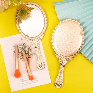 Ornate vintage gold handheld makeup mirror with elegant embossed floral pattern on yellow background