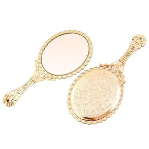 Vintage rose gold handheld makeup mirror with intricate floral pattern on white background