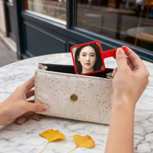 Portable square red handheld makeup mirror shown being taken out of a white glittery purse