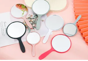 Assorted colors of handheld circular makeup mirrors with plastic handles on pink background