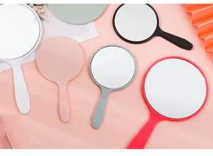 Close-up of various colorful round handheld makeup mirrors displayed on a pink background