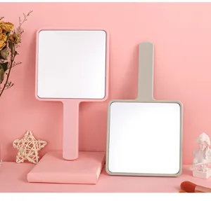 Large square handheld makeup mirrors in pink and grey displayed with aesthetic props