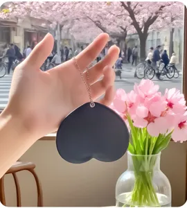 Close-up of a handheld dark gray heart-shaped portable mirror with a delicate metal chain