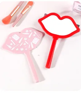 Close-up of pink and red lip-shaped hand mirrors with makeup brushes on white background