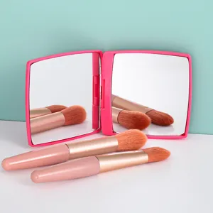 Tragbarer rosa Klappspiegel mit Make-up-Pinseln auf einem stilvollen zweifarbigen Grund.