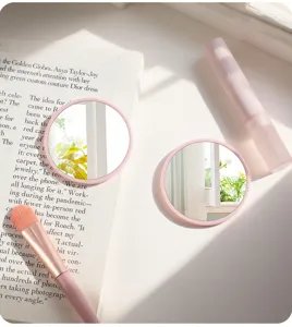 Close-up of two pink circular portable makeup mirrors in a bright sunny lifestyle scene