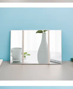 Detailed side view of tri-fold portable makeup mirror on a minimalist light blue desktop