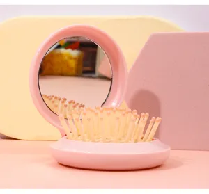 Close-up of pink foldable hairbrush with integrated mirror and soft massage bristles