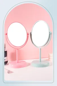 Close-up of pink and mint green rotatable oval desktop makeup mirrors in a studio setting.