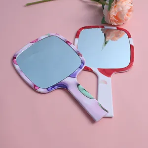 Detailed view of two square handheld makeup mirrors with colorful floral patterns on pink background
