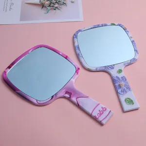 Detail view of purple floral and pink marble handheld makeup mirrors on pink background