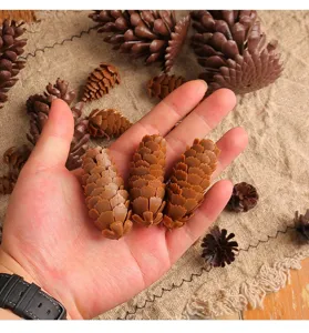 Close-up view of three artificial plastic spruce pine cones held in a hand for scale