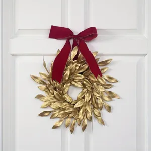 Elegante corona de Navidad con hojas doradas y lazo de terciopelo rojo en puerta blanca.