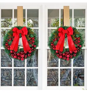 Traditionele kerstkransen met rode bessen en strikken op een elegant wit venster