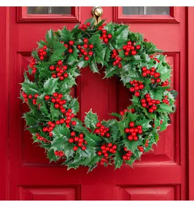 Detailed view of artificial Christmas holly wreath hanging on a classic red wooden door