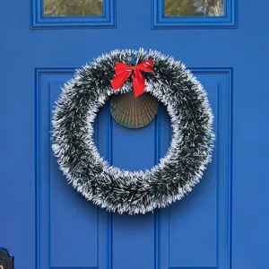 Festive 25-30cm white and green tinsel Christmas wreath with a red bow on a blue door