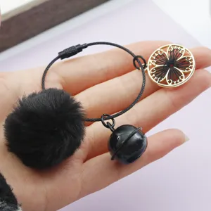 Gros plan d'un pompon noir et d'une clochette tenus en main pour la création de bijoux DIY