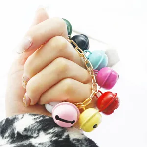 Détail d'un bracelet de cloches colorées fait main tenu à la main avec chaîne dorée.