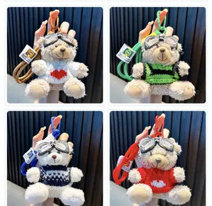 Macro view of four varieties of plush bear keychains wearing goggles and cute sweaters