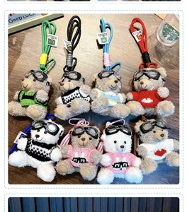 Eight plush bear keychains wearing goggles and colorful sweaters on a wooden desk
