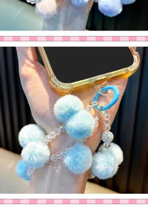 Close-up of fluffy blue pom-pom and beaded phone strap hanging from a smartphone case