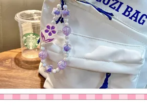Close-up view of a luminous purple flower beaded charm hanging on a white backpack.
