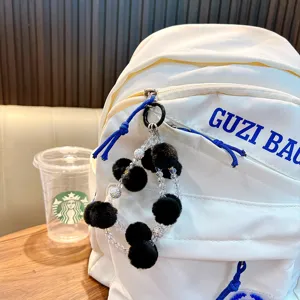 Handmade double chain phone strap with black pom-poms and clear beads on a white backpack