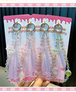 Nahaufnahme von irisierenden Kristall-Handyketten mit Wolkenanhängern auf rosa Karten-Displays.