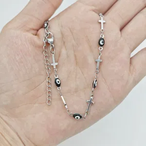 Detailed view of stainless steel necklace with cross and evil eye enamel charms.