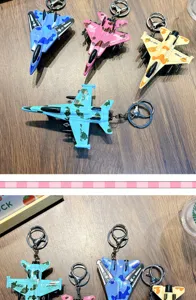 Dettaglio di portachiavi a forma di caccia in lega mimetica in vari colori su tavolo in legno