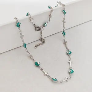 Detailed view of stainless steel cross and green enamel evil eye charms on a silver chain.