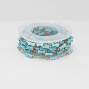 Detail of blue bamboo-shaped acrylic beads and gold stainless steel chain on a spool
