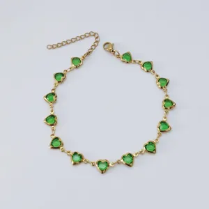 Detailed macro view of gold stainless steel anklet with vibrant green heart-shaped crystals