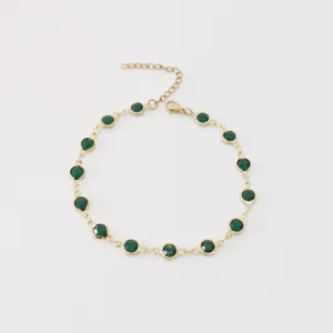 Detail of a stainless steel gold-plated anklet featuring elegant round green glass gems.