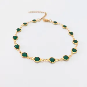 Close-up detail of a gold-plated stainless steel anklet with emerald green glass beads