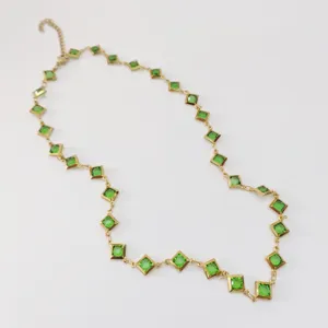 Close-up view of a gold-toned necklace featuring vibrant green square cut gemstones