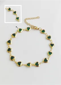 Detailweergave van hartvormige groene kristallen bedeltjes aan een gouden rvs enkelbandje.