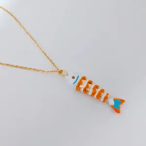 Detalle de collar de acero inoxidable dorado con un vibrante colgante de pez móvil esmaltado.