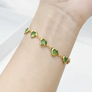 Detailansicht eines goldenen Herzarmbands mit grünen Glasanhängern am Handgelenk.