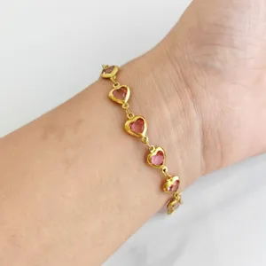 Detailed close-up of a gold heart bracelet with pink gems worn on a woman's wrist.