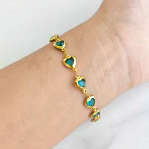 Close-up detail of a golden stainless steel bracelet with heart-shaped blue gemstones.