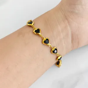 Detailed view of a gold heart bracelet with black inlays worn on a woman's wrist.
