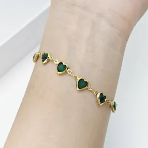 Detailansicht eines goldenen Herzarmbands mit smaragdgrünen Glassteinen am Handgelenk