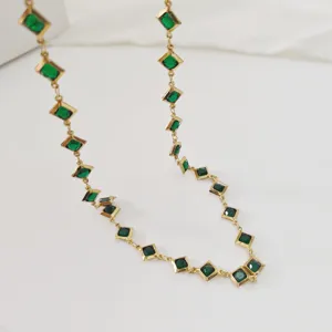 Close-up of elegant gold stainless steel necklace with green rhombus-shaped crystals.