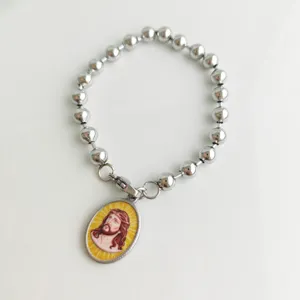 Close-up detail of a silver stainless steel bead bracelet with an oval Jesus pendant.