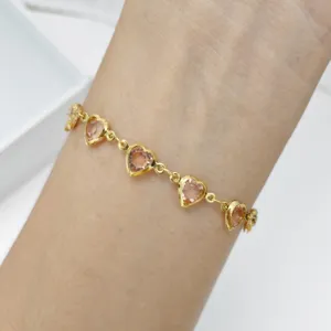 Nahaufnahme eines goldenen Herzarmbands mit rosa Glassteinen am Handgelenk getragen.