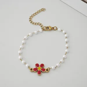 Detail of golden stainless steel bracelet with white imitation pearls and red daisy charm