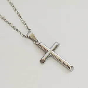 Detailed macro view of a polished silver stainless steel cross pendant on a thin chain