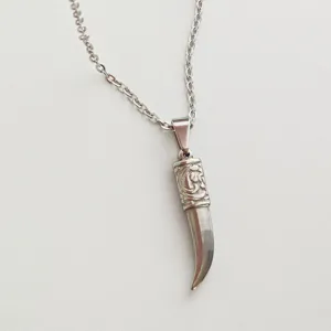 Close-up of stainless steel fang necklace pendant with embossed scroll patterns