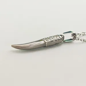 Close-up detail of a vintage stainless steel fang pendant with embossed pattern.